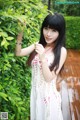 A woman in a white dress standing next to a bush.