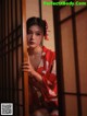 A woman in a red kimono leaning against a wooden door.