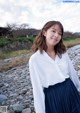 A woman in a white shirt and blue pleated skirt posing for a picture.