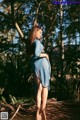 A pregnant woman in a blue dress standing in the woods.