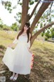 A woman in a white dress standing next to a tree.