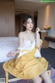 A woman in a yellow dress sitting on a bed.