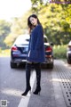 A woman in a blue sweater and black boots standing on a street.