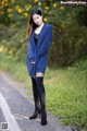 A woman in a blue sweater and black boots standing on a road.