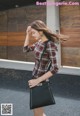 A woman in a plaid shirt is holding a black bag.