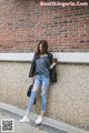 A woman leaning against a brick wall holding a drink.