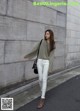 A woman wearing white jeans and a green shirt is walking down the street.