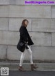 A woman in white jeans and a black coat is walking down the street.