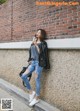 A woman leaning against a brick wall drinking a drink.