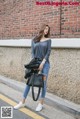 A woman is standing in front of a brick wall.