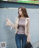 A woman wearing a beige jacket and jeans standing next to a wall.