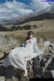 A woman in a white dress sitting on a rock.