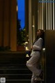 A woman in a white suit leaning against a wall.