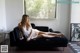 A woman sitting on a black couch in a white dress.