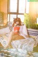 A woman sitting on a bed with a cat on her head.