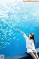 A woman sitting on a ledge in front of a large aquarium.